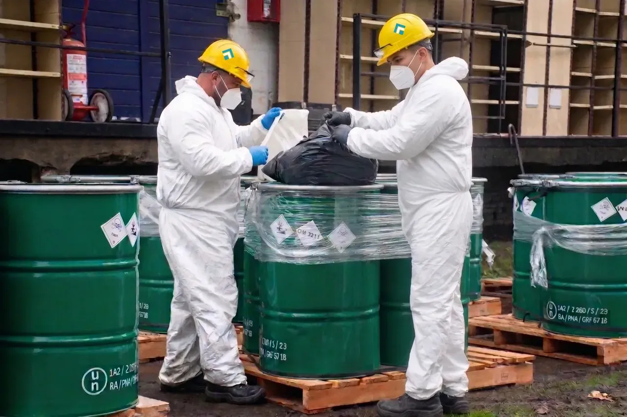 Operarios con trajes Tyvek y cascos amarillos manipulando tambores industriales con etiquetado UN